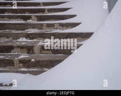 Vecchi gradini in cemento di una scalinata spazzata dalla neve durante una nevicata in una giornata invernale. Foto Stock