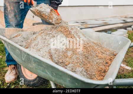 Un lavoratore mescola cemento con sabbia direttamente in una costruzione carriola - preparazione della miscela Foto Stock