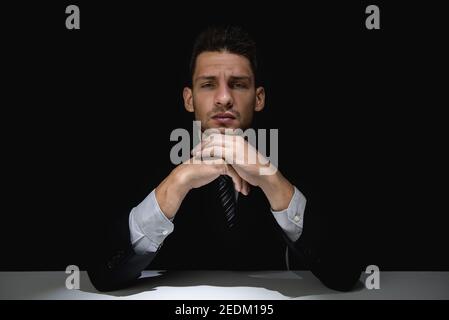 Meditare l'uomo in tuta nera con le mani sul mento ombra scura che si proiettata verso la fotocamera Foto Stock