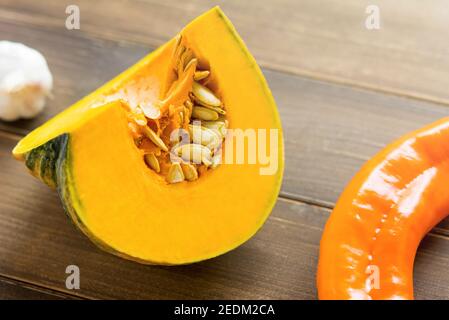 Zucca gialla, carne e semi freschi, grezzi, a fette, su tavola di legno con altri ingredienti alimentari preparati per la cottura Foto Stock