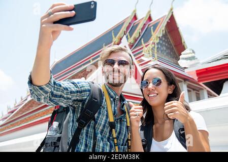 Giovane coppia turistica backpackers prendendo selfie da smartphone a antico Tempio tailandese sulle vacanze estive a Bangkok Thailandia Foto Stock