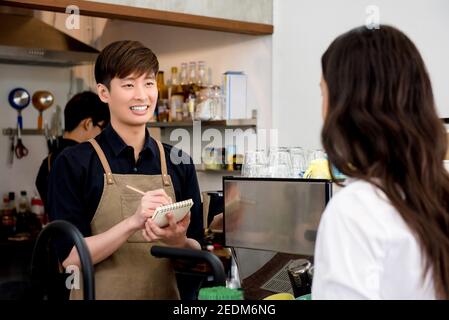 Giovane uomo asiatico personale che prende ordine da donna cliente a. il banco della caffetteria Foto Stock