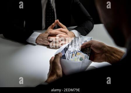 Uomo d'affari che controlla i soldi, dollari USA, nella busta appena data dal suo socio - concetti di corruzione e di corruzione Foto Stock