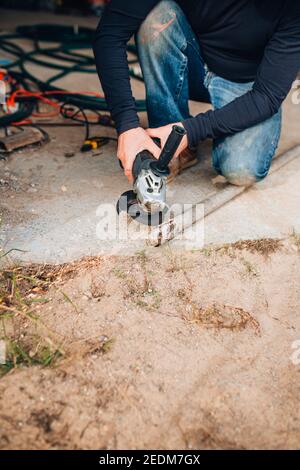 Un uomo ripara un attrezzo in un garage - tagli metallo con una smerigliatrice - scintille da taglio mosca Foto Stock