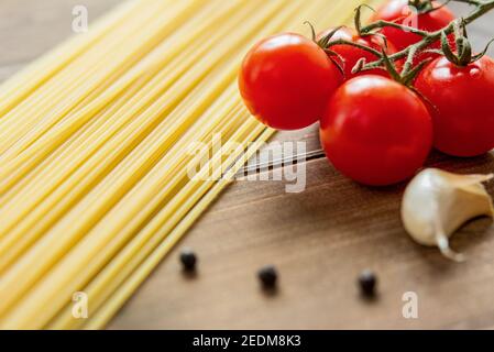 Ingredienti alimentari, spaghetti crudi con pomodori rossi, aglio e pepe su tavola di legno preparato per la cottura Foto Stock