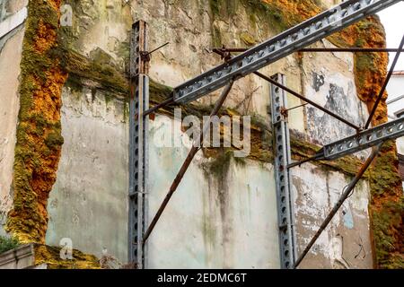 Vecchia parete mussosa danneggiata di un edificio distrutto sigillato con schiuma, sostenuta da travi di montaggio in acciaio Foto Stock