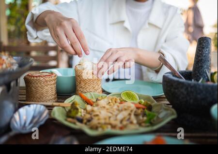 Donna che apre contenitore di bambù appiccicoso di riso mentre ha tre Pasto di portata in un guardaroba di ristorante tailandese Foto Stock
