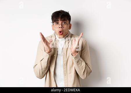 Ritratto di hipster ragazzo sorpreso in occhiali che controlla promo impressionante, dire WOW e gasting stupito, alzando le mani in su con incredulità, in piedi sopra Foto Stock