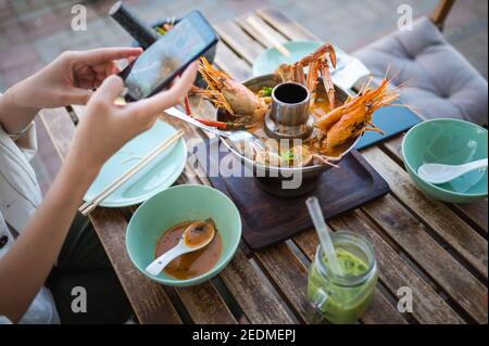 Donna che scatta foto di una zuppa tailandese Tom Yum con gamberi e granchio mentre si cena in un ristorante Foto Stock