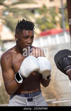 Il pugile nero professionista allena il principiante nero del boxer con i mittens e i guanti di boxing un codice categoria di boxing all'aperto in una giornata soleggiata mentre entrambi sudano. Foto Stock