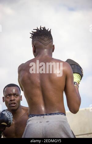 Il pugile nero professionista allena il principiante nero del boxer con i guanti di boxing una classe di boxing all'aperto in una giornata soleggiata mentre entrambi sudano. Concetto di boxe Foto Stock