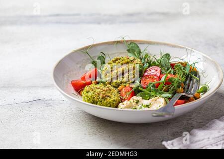 Insalata di falafel con pomodori, hummus e noccioline di piselli in una ciotola grigia. Concetto di cibo basato su piante. Foto Stock