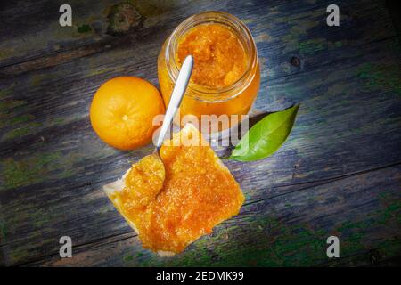 Marmellata d'arancia fresca pura con cucchiaio inclinato su pane spalmato con lenza d'arancia come ornamento. Copia spazio su entrambi i lati Foto Stock
