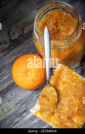 Marmellata d'arancia fresca pura su pane spalmato con cucchiaio inclinato in posizione verticale. Copia spazio Foto Stock