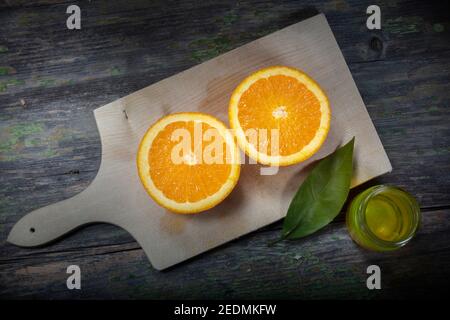 Foto macro di Still Life. ​​Oranges a metà fette su un tagliere. Vasetto piccolo di olio d'oliva e di arancia lasciare come decorazione Foto Stock
