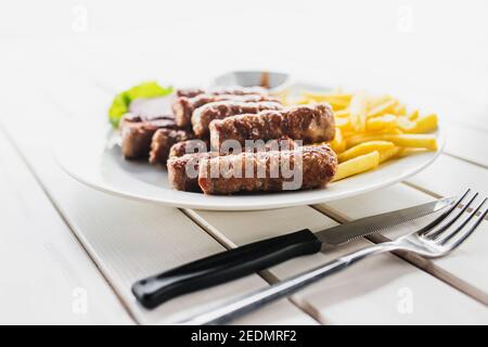 Salsicce fritte con spicchi di patate su un piatto bianco - pranzo abbondante - terrazza aperta affacciata sul mare Foto Stock