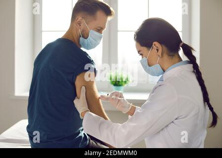 Infermiera che dà il vaccino al paziente maschile in un ufficio soleggiato di clinica moderna o ospedale Foto Stock