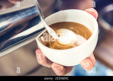 Barista professionista che versa il latte in cottura a vapore in una tazza di caffè e prepara il latte arte Foto Stock