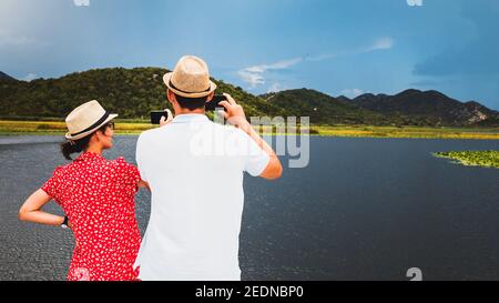 Uomo e donna scattano foto di paesaggi su smartphone - coppia sposata in vacanza - social network post foto Foto Stock