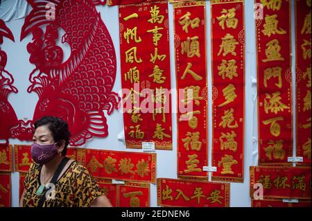 29.01.2021, Singapore, , Singapore - UNA donna che indossa una maschera facciale si erge davanti a bandiere con personaggi cinesi venduti come decorazioni e buona fortuna Foto Stock