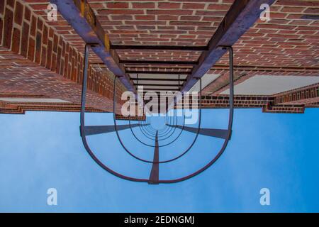 Immagine in basso su delle scale di fuga dal fuoco metallico all'esterno di un edificio industriale rustico in mattoni di pietra con cielo blu Foto Stock