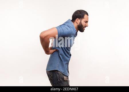 Vista laterale esausto uomo porticato malsano che tocca la schiena dolorante, che soffre di disagio lombare inferiore, dolore muscolare, disco ferito della colonna vertebrale. Riprese in studio al coperto Foto Stock