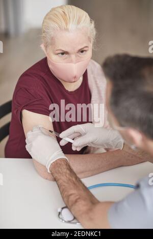 Ritratto di medico irriconoscibile vaccinare donna anziana indossando maschera contro covid 19 Foto Stock