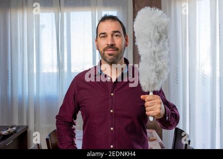 Uomo bearded in una camicia viola che si presenta divertente con un pulitore. Concetto di pulizia Foto Stock