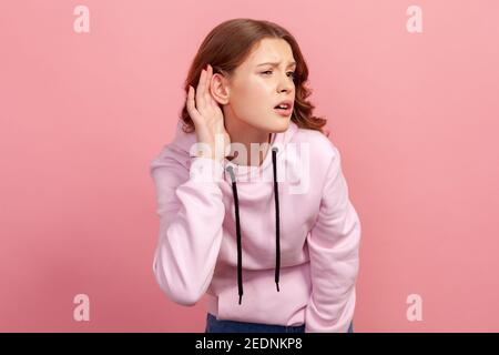 Ritratto di bruna attenta ragazza teen in felpa con cappuccio tenendo la mano vicino all'orecchio cercando di ascoltare conversazione tranquilla, sorso di udito. Riprese in studio al coperto, Foto Stock