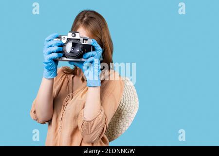 Una bionda in guanti medici lattice sta scattando foto con una macchina fotografica vintage su uno sfondo con un posto per la pubblicità. Foto e hobby durante un Foto Stock