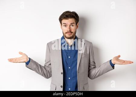 Non lo so. Uomo d'affari confuso si diffonde le mani lateralmente e guardare indeceless, cant aiuto, non hanno idea, in piedi su sfondo bianco nel vestito Foto Stock