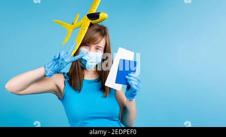 Banner. Una bambina bionda in una maschera medica e guanti protettivi, un aereo giocattolo illuminante sulla testa, un passaporto e biglietti aerei. Sognare di viaggiare su un Foto Stock