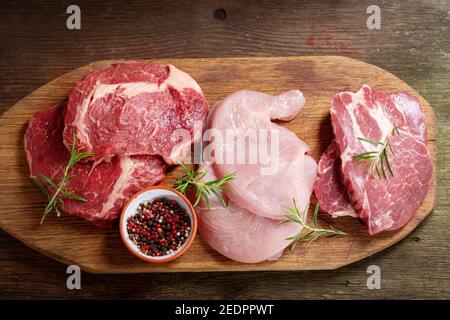 vari tipi di bistecche di carne fresca: manzo, maiale e tacchino su tavola di legno, vista dall'alto Foto Stock