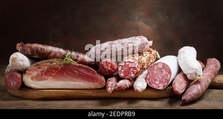 Vari tipi di salame, speck e salsicce su un tavolo di legno Foto Stock
