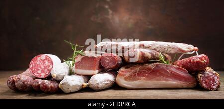 Vari tipi di salame, speck e salsicce su un tavolo di legno Foto Stock