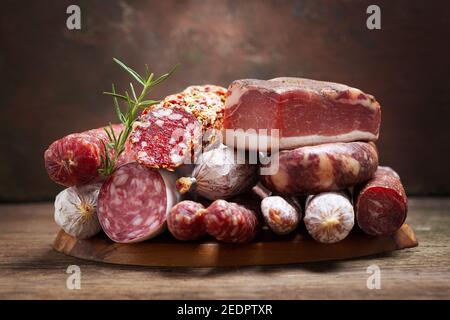 Vari tipi di salame, speck e salsicce su tavola di legno Foto Stock
