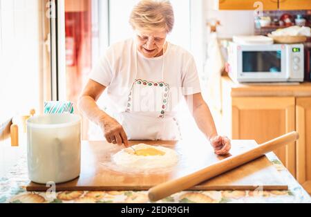 Donna felice che prepara ricevuta fatta a mano alla cucina della casa - locale Concetto alimentare con preparazione di pasta italiana fatta in casa - calda filtro per retroilluminazione luminosa Foto Stock