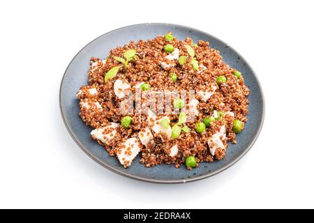 Porridge di quinoa con piselli verdi e pollo su piastra di ceramica isolato su sfondo bianco. Vista laterale, primo piano. Foto Stock