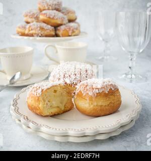 Ciambelle con glassa e cocco e ripieno di budino al cioccolato bianco. Dolci appetitosi su un piatto bianco. Foto Stock