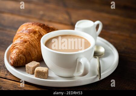 Croissant e tazza di caffè con latte su vecchio tavolo di legno, vista closeup. Colazione continentale o pausa caffè nel caffè Foto Stock