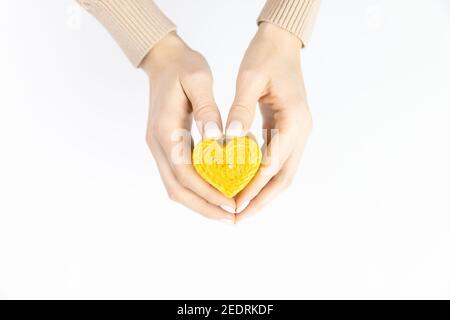 Candela di cera d'api a forma di cuore in mani femminili su sfondo bianco. Foto Stock