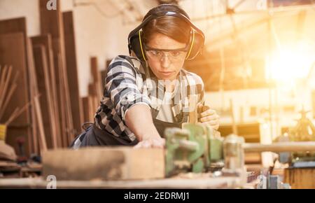 La giovane donna si sta allenando per essere una falegname in officina mentre si lavora con legno Foto Stock