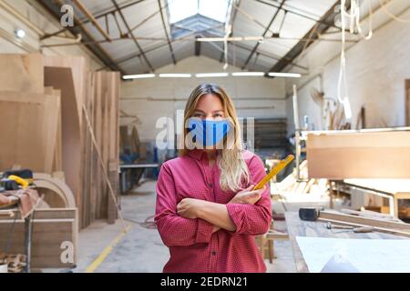 Donna come apprendista artigiano con maschera facciale a causa di Covid-19 in officina Foto Stock