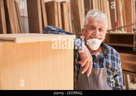 Artigiano senior come maestro con maschera facciale a causa di Covid-19 nella falegnameria Foto Stock