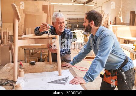 Artigiano senior lavora con morsetto a vite su una sedia con apprendista falegname Foto Stock