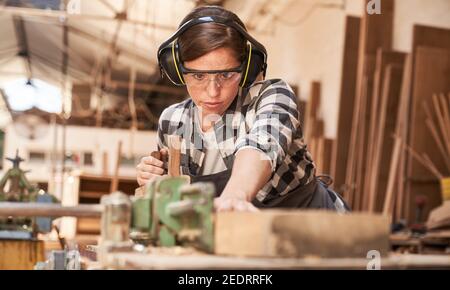 La giovane donna lavora come un falegname o un artigiano in un officina con legno Foto Stock