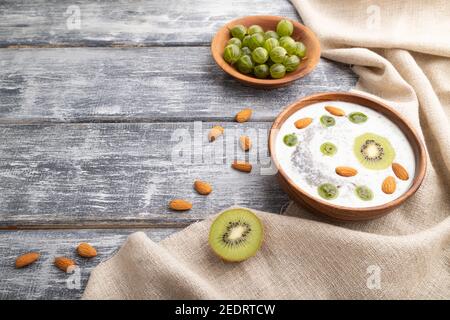 Yogurt con kiwi, uva spina, chia e mandorle in ciotola di legno su fondo grigio di legno e tessuto di lino. Vista laterale, spazio di copia. Foto Stock