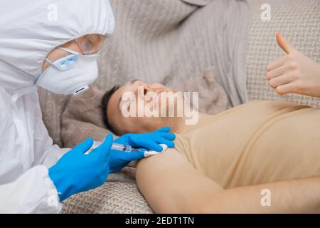 Uomo felice che ottiene il vaccino covid-19 da un lavoratore medico che indossa maschera e guanti. Coronavirus e concetto di vaccinazione. Foto Stock