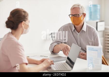 Ritratto di uomo anziano che indossa maschere mentre si parla con il medico o l'infermiere in clinica medica, copia spazio Foto Stock