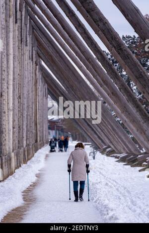 13 febbraio 2021, Sassonia-Anhalt, Schönebeck: Una donna sulle stampelle cammina lungo la casa di laurea coperta di neve a Schönebeck-SALZELMEN. Uno speciale processo di evaporazione arricchisce l'aria nelle immediate vicinanze dei lavori di graduazione di 320 metri di lunghezza e 17 metri di altezza con i minerali, in modo che possa alleviare i disturbi respiratori. SALZELMEN è la più antica stazione termale in Germania. Foto: Stephan Schulz/dpa-Zentralbild/ZB Foto Stock